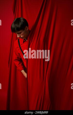 giovane uomo tenace con una camicia vivace con bretelle nascoste dietro una tenda rossa, look alla moda Foto Stock