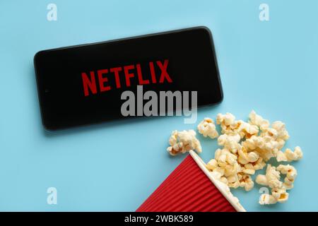 Smartphone con logo Netflix e popcorn su sfondo blu. Netflix è specializzata e fornisce contenuti multimediali in streaming e video on demand online e DVD by Foto Stock