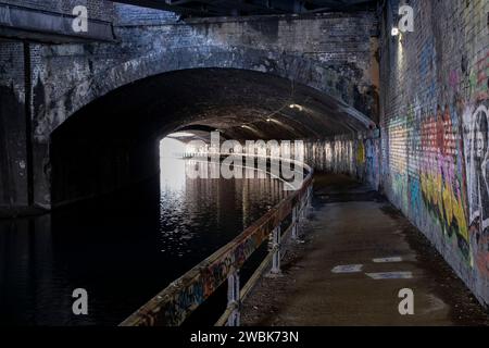 Graffiti lungo il lungo tunnel curvo in mattoni sotto le linee ferroviarie sul Digbeth Branch Canal nel centro della città il 9 gennaio 2024 a Birmingham, Regno Unito. Birmingham ha circa 35 km di canali, che si dice essere più che a Venezia, e sono molto un ricordo di un patrimonio industriale di Birminghams. Durante la Rivoluzione industriale questi canali erano occupati, trasportando merci pesanti come carbone, ferro, mentre giocavano un ruolo fondamentale nello sviluppo di Birmingham come potenza industriale. Foto Stock