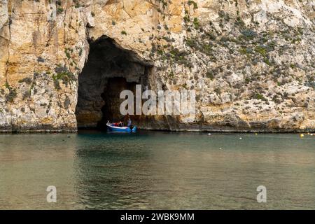 Dwejra, Malta - 19 dicembre 2023: pescatore che trasporta i turisti attraverso l'arco naturale del Mare interno sull'isola di Gozo a Malta in un tour in barca Foto Stock