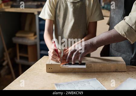 Primo piano del bambino che misura con attenzione la tavola di legno in officina con l'aiuto dell'insegnante, copia spazio Foto Stock