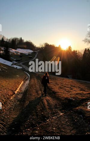 Giovane donna al tramonto con vista su Wamberg, chiesa di St Anna, distretto di Garmisch-Partenkirchen, Werdenfelser Land, alta Baviera, Baviera, Germania, primavera, Europa Foto Stock