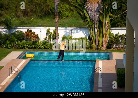 Vista dall'alto di un lavoratore che pulisce una piscina in una casa privata in estate. Foto Stock