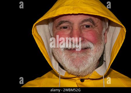 Un marinaio in pensione, sorridente e pieno di gioia sotto il suo cappuccio giallo, pronto per la prossima avventura sulla terraferma! Foto Stock