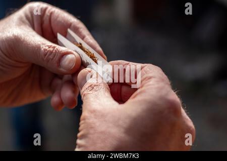 Le mani di un uomo che gira una sigaretta, la carta sul tabacco Foto Stock