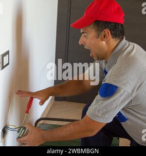 Immagine di un elettricista mentre installa una spina elettrica e riceve una scossa elettrica. Sicurezza del lavoro Foto Stock