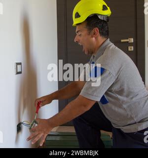 Immagine di un elettricista mentre installa una spina elettrica e riceve una scossa elettrica. Sicurezza del lavoro Foto Stock