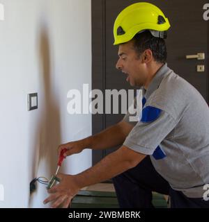 Immagine di un elettricista mentre installa una spina elettrica e riceve una scossa elettrica. Sicurezza del lavoro Foto Stock