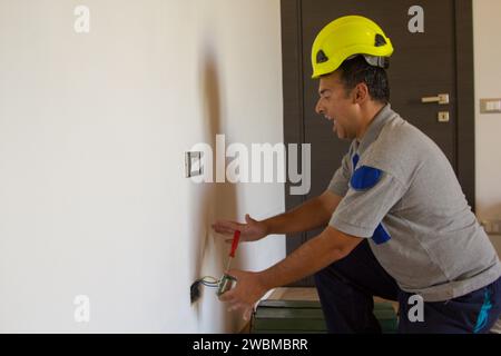 Immagine di un elettricista mentre installa una spina elettrica e riceve una scossa elettrica. Sicurezza del lavoro Foto Stock