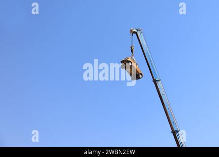 Una gru che solleva un'auto arrugginita contro un cielo blu. Foto Stock