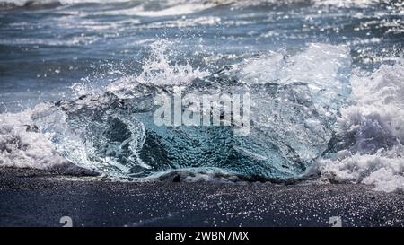 Un blocco di ghiaccio limpido con sacche d'aria viene lavato dalle onde sulle sabbie nere di Diamond Beach in Islanda. Foto Stock