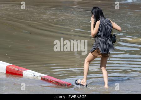 Una donna con un telefono salta con attenzione attraverso una strada allagata, Bangkok, Thailandia Foto Stock