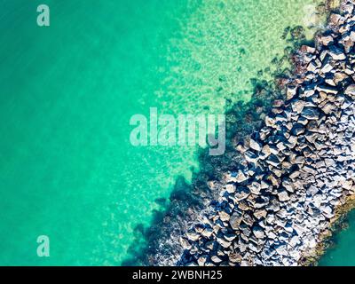 Vista aerea dell'acqua dell'oceano verde smeraldo accanto a un molo roccioso Foto Stock