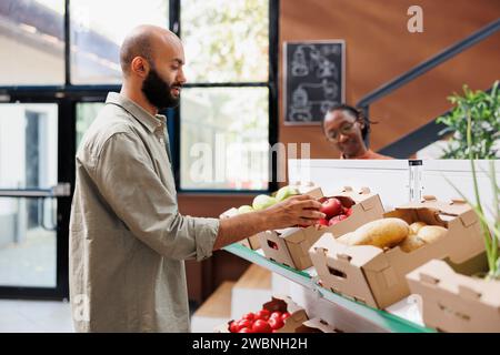 Un cliente di sesso maschile che cerca frutta e verdura coltivate localmente. L'uomo del Medio Oriente raccoglie mele rosse appena raccolte dalle scatole sugli scaffali del supermercato ecologico. Foto Stock