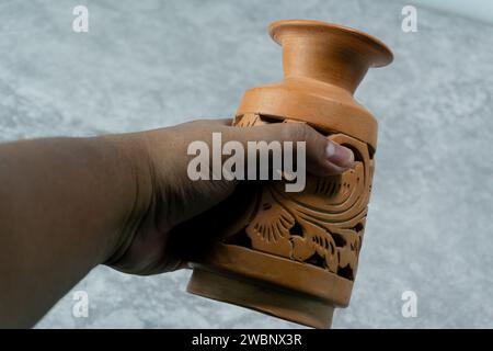 Una caraffa in argilla con rilievi laterali è tenuta in mano e posizionata su un tavolo grigio con una trama in cemento Foto Stock