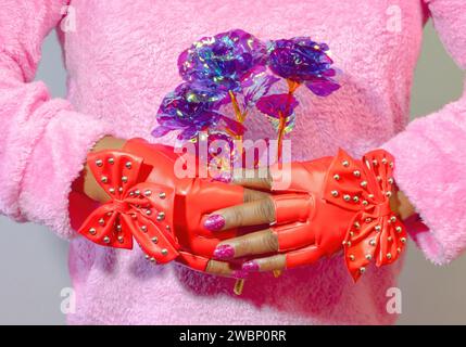 Una diversa donna afroamericana che indossa guanti rossi con borchie e regge un mazzo di fiori viola iridescenti e olografici Foto Stock