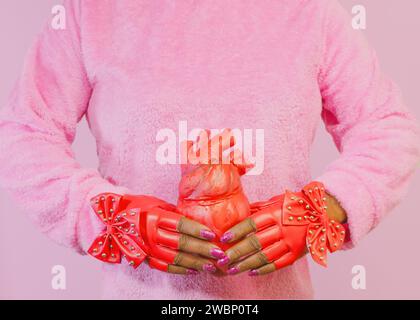 Una donna afroamericana diversa che indossa guanti rossi con borchie e tiene un cuore anatomico rosso Foto Stock