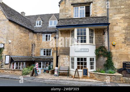 Chipping Campden, strada principale inferiore in questa città commerciale con il negozio di panetteria Huxleys e il negozio di barbieri adiacente, Gloucestershire, Inghilterra, Regno Unito, 2023 Foto Stock