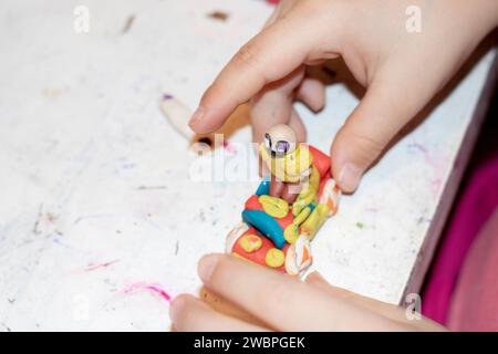 Primo piano: Un bambino che prepara una persona in argilla colorata su un tavolo bianco Foto Stock