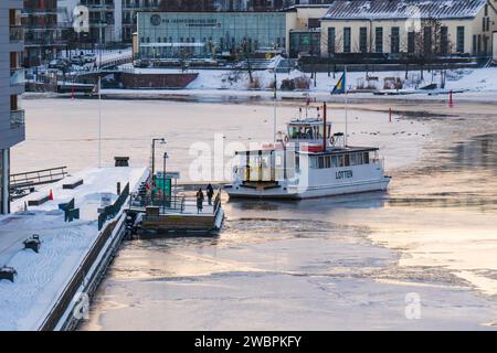 Ghiaccio sul mare a Henriksdal e Hammarby Sjöstad vicino a Stoccolma, Svezia, traghetto per pendolari linea 1 da Luma a Djurgården rompendo il ghiaccio. Cielo arancione. Foto Stock