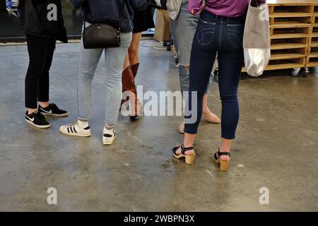 Gambe e scarpe, runner e sneakers stivali e jeans, cinque donne in piedi in una galleria d'arte aperta con pavimento in cemento lucido Foto Stock