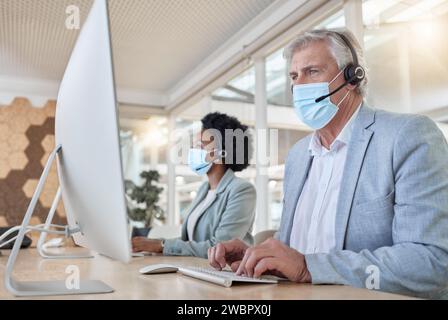 COVID, dipendenti dell'help desk con maschera al computer e uomo maturo e donna nera nel call center. Conformità dell'ufficio, team di consulenza online nel coworking Foto Stock