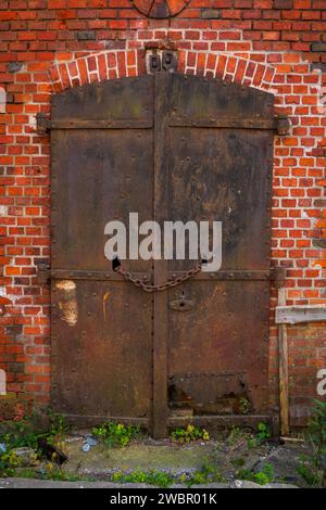 Porte di metallo arrugginite su un muro di mattoni, chiuse con una catena, che accennano alla storia e al mistero. Foto Stock