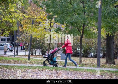 Giovane genitore (mamma) che porta il suo bambino al parco pubblico per bambini in autunno a ottobre Foto Stock