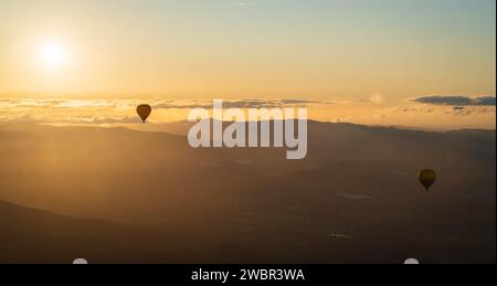 Una vibrante scena di mongolfiere che scivolano sopra le maestose cime delle montagne all'alba Foto Stock