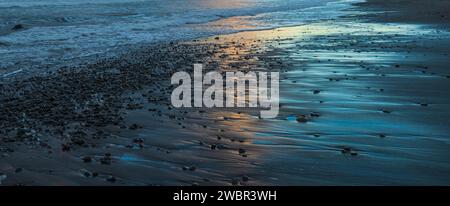 Un'alba mozzafiato su una spiaggia tranquilla, che getta una calda luce dorata sui ciottoli lisci Foto Stock