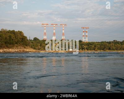 Enormi alberi di trasmissione di potenza che torreggiano sopra la foresta e un ampio fiume con sponde rocciose Foto Stock