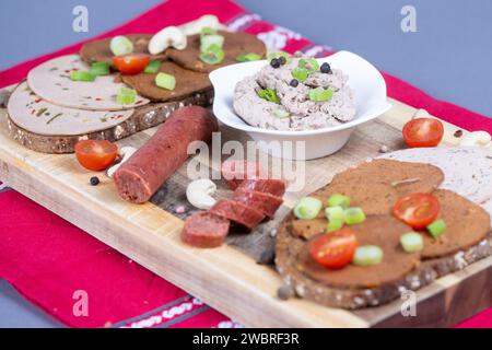 Dresda, Germania. 6 gennaio 2024. Fette di pane condite con varie salsicce vegane, una salsiccia all'aglio vegan e una ciotola con un'alternativa di salsiccia al fegato vegan a base di piselli su una tavola di legno. Credito: Sebastian Kahnert/dpa/Alamy Live News Foto Stock