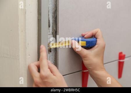 Donna che piastrella le pareti del bagno, utilizzando un metro a nastro per misurare la lunghezza. Processo di installazione delle piastrelle nel bagno passo dopo passo. Miglioramento fai da te Foto Stock