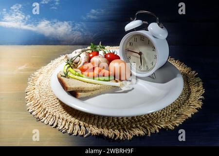 Digiuno intermittente, piatto con sveglia e parzialmente riempito di cibo, concetto di dieta a intervalli di un terzo del giorno, indietro Foto Stock