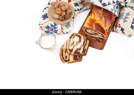 Cozonac, tradizionale pane dolce rumeno con ripieno di noci, a fette, con un bicchiere di latte e un panno modellato, piatto Foto Stock