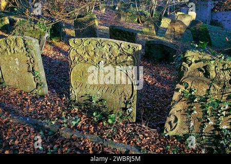 Il sole invernale nel tardo pomeriggio mette in risalto i dettagli decorati su vecchie lapidi intemprate in un cimitero della chiesa. Foto Stock