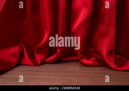 Pavimento in legno vuoto con eleganti tende in tessuto satinato rosso ondulato, sfocate sullo sfondo, posizionamento del prodotto Foto Stock