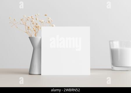 Mockup con carta di invito quadrata con decorazione gypsophila sul tavolo beige. Foto Stock