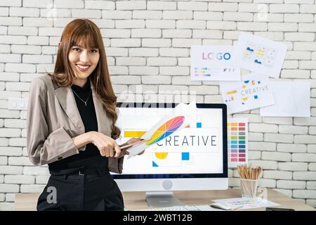Una giovane graphic designer asiatica che lavora in un ufficio creativo e dinamico Foto Stock