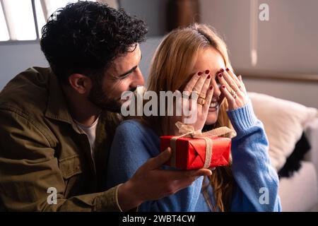 Un giovane sorprende il suo partner facendogli un regalo in una scatola rossa. Festa di San Valentino Foto Stock