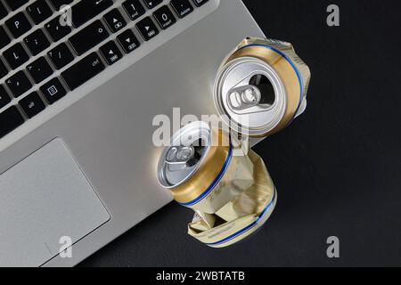 Lattine di birra in alluminio schiacciato sulla tastiera di un computer portatile. Vista superiore con spazio di copia. Alcol e aggressione sui social network Foto Stock