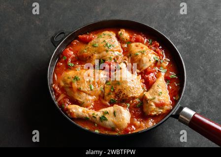 Stufato di pollo georgiano con pomodori ed erbe (chakhokhbili) in padella di ghisa su fondo di pietra scura. Pollo al forno con sugo di verdure al pomodoro. Foto Stock