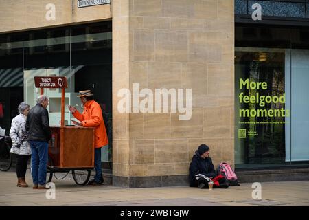 Sebbene conosciuta per la sua prestigiosa università, Cambridge è anche una delle città più disuguali del Regno Unito. C’è un’allarmante disparità tra “città e abito” in termini di ricchezza. La fotografia mostra un senzatetto che implora con un cartello che lo indica "More Feel Good Moments". Foto Stock