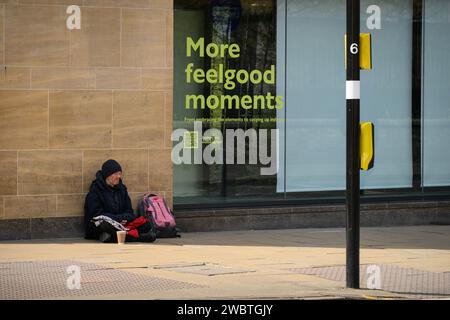 Sebbene conosciuta per la sua prestigiosa università, Cambridge è anche una delle città più disuguali del Regno Unito. C’è un’allarmante disparità tra “città e abito” in termini di ricchezza. La fotografia mostra un senzatetto che implora con un cartello che lo indica "More Feel Good Moments". Foto Stock