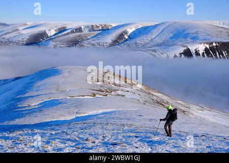 Drumochter, Scozia, Regno Unito. 12 gennaio 2024. Neve sui munros e inversioni di nuvole intorno alle valli di Drumochter attirando gli escursionisti per le passeggiate impegnative e creando panorami spettacolari. Escursionista che scende A ' Mharconaich con un'inversione di nuvole sul percorso principale A9 attraverso il passo di Drumochter, e una vista verso i munros orientali di Drumochter. Crediti: Craig Brown/Alamy Live News Foto Stock