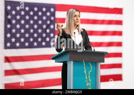 Donna professionista che tiene un discorso su un piedistallo e gestisce con un dito davanti a una bandiera americana Foto Stock
