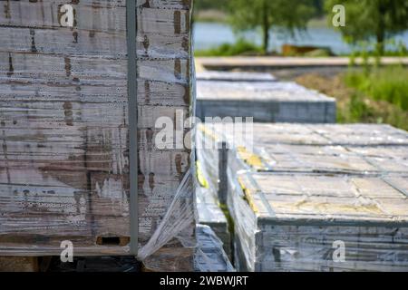 Pallet con lastre di pavimentazione grigie su fondo di erba verde. La confezione in plastica protegge la piastrella dagli effetti atmosferici. Preparazione per l'installazione Foto Stock