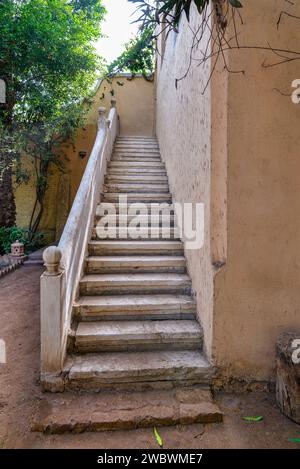 Set di gradini in pietra ben consumati che confinano con una parete intonacata, che conducono a una destinazione invisibile all'interno di un tranquillo giardino, inondato di luce soffusa Foto Stock