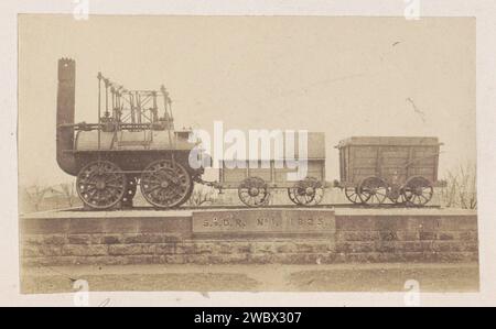 Locomotiva con rimorchi su un piedistallo, anonimo, 1878 - 1890 la fotografia su una base di mattoni è una locomotiva a vapore con un tender per acqua e carburante e un carro. Sotto il testo è stato scolpito: 'S. & D.R. No. 1. 1825. '. Questo si riferisce alla Locomotion No. 1., la prima locomotiva che guidò sul percorso della Stockton and Darlington Railway (S. & D.R.) e fu costruita da George Stephenson (1781-1848). Parte dell'album di viaggio città europee, presumibilmente svedesi. Locomotiva a vapore con stampa albumen di supporto fotografico Darlington. monumento, statua Darlington Foto Stock