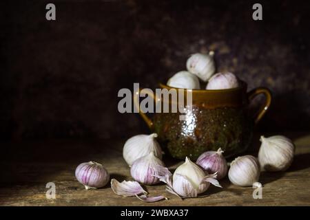 Aglio fresco a guanto singolo o aglio perlato o aglio solo, varietà di ampeloprasum Allium con una pentola per spezie su sfondo scuro - scuro e lungoso Foto Stock